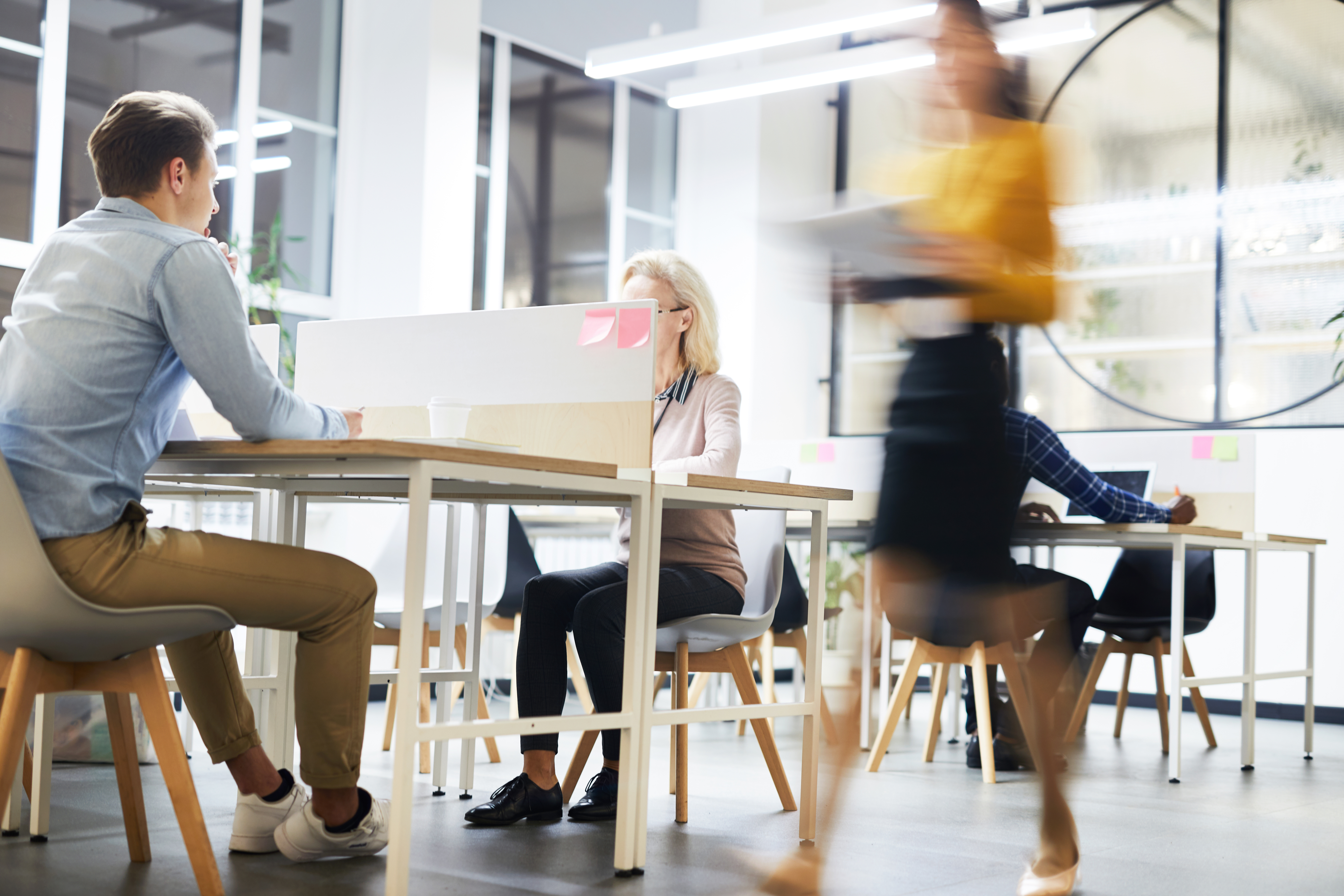 Image of an office with workers at desks and a woman walking at a brisk pace